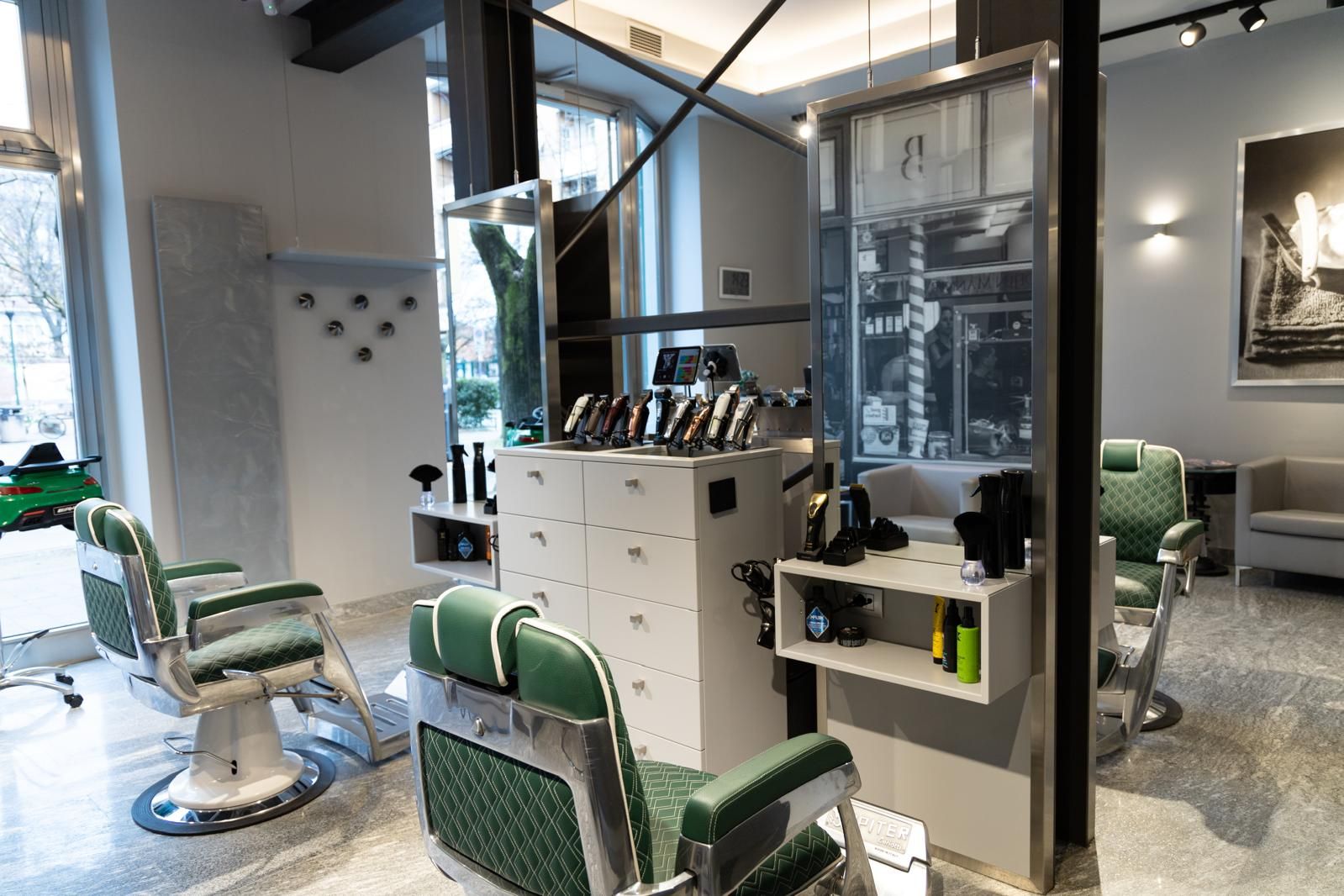 Il salone: poltrone da barbiere in pelle verde, specchi sospesi e le postazioni con i rasoi